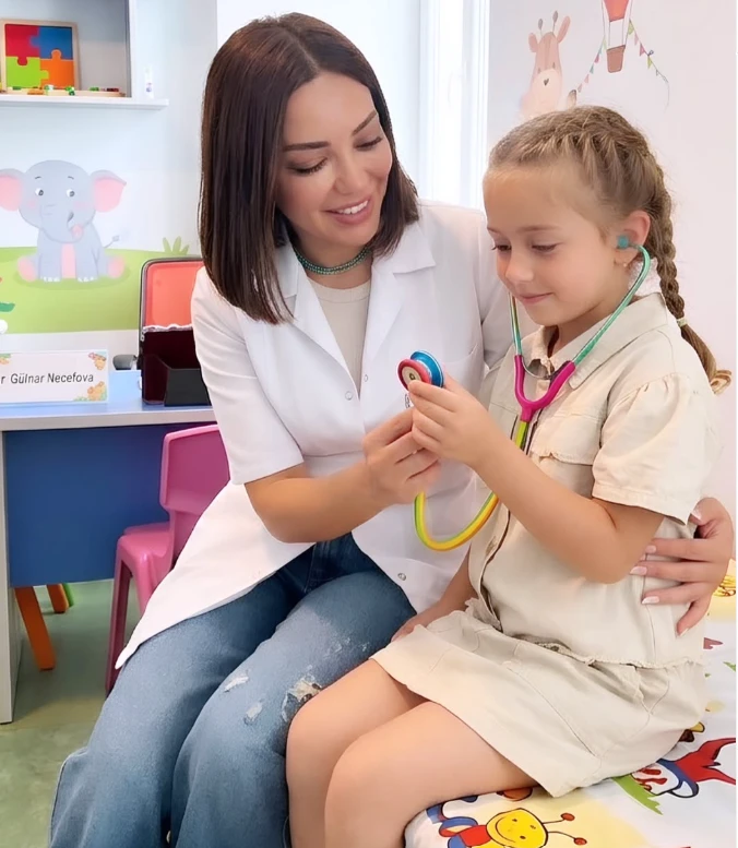 Gülnar Nəcəfova pediatriya otağında balaca qıza stetoskopu göstərir